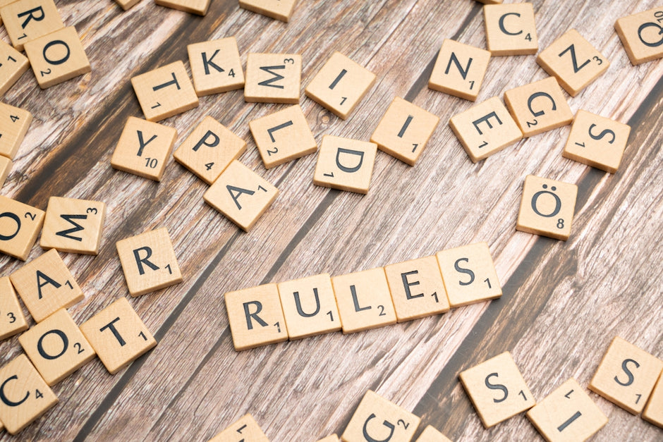 scrabble tiles spelling rules on a wooden surface