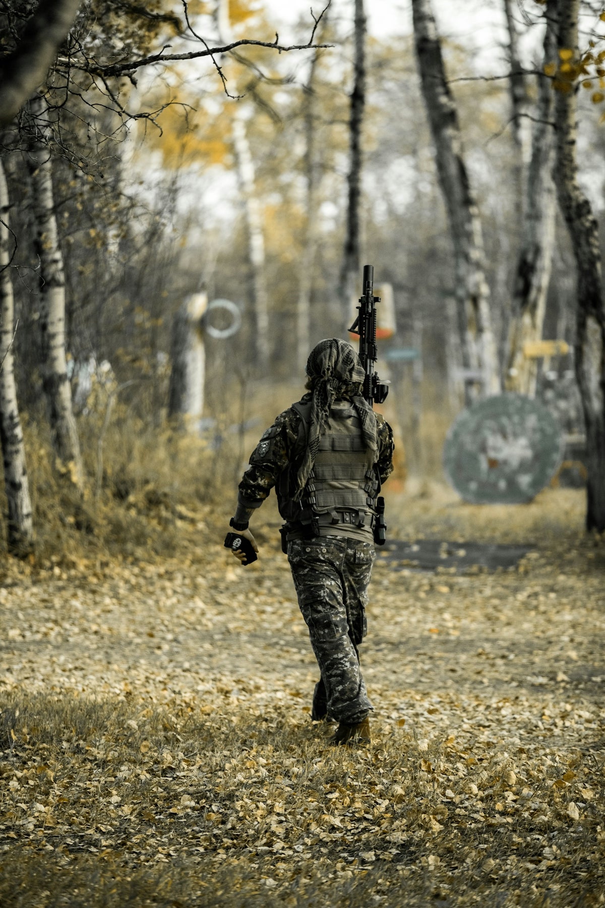Camouflaged person with rifle walking through autumn woods
